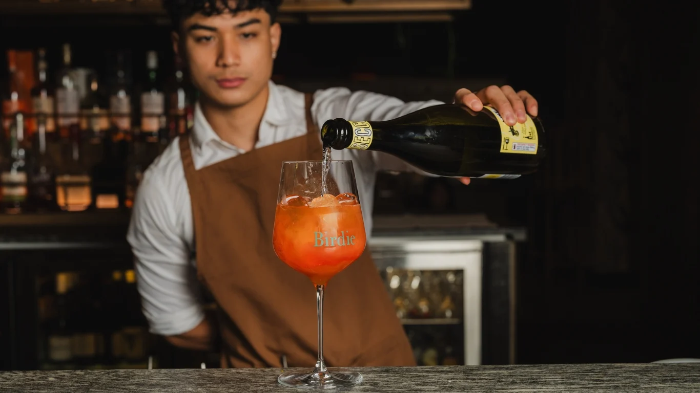 Bartender pouring prosecco into a spritz in a Birdie-branded wine glass at Birdie Bar & Brasserie, Sydney CBD