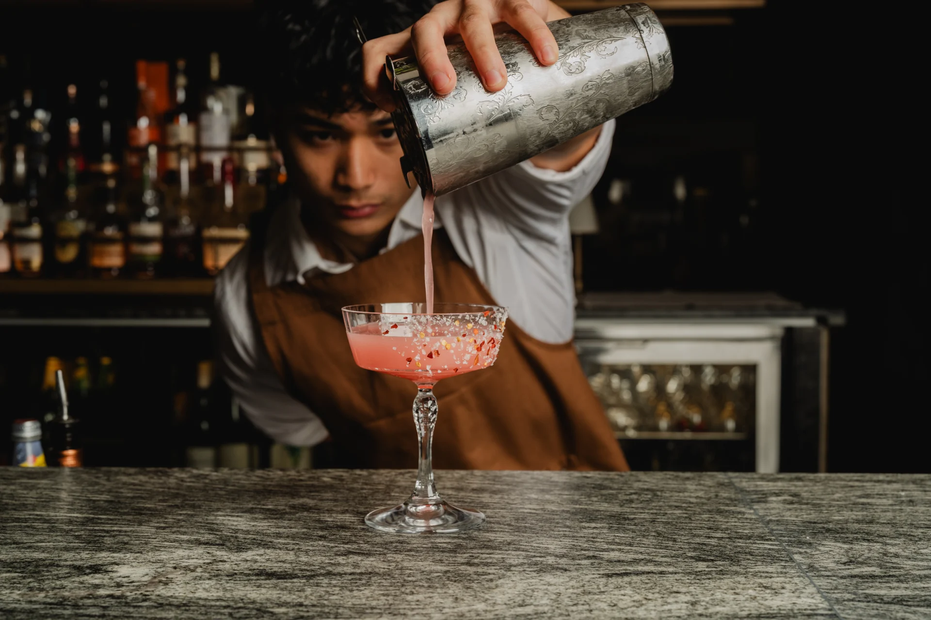 Bartender pouring a pink cocktail into a garnished coupe glass at Birdie Bar & Brasserie.